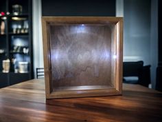 an empty wooden frame sitting on top of a wooden table in front of a book shelf