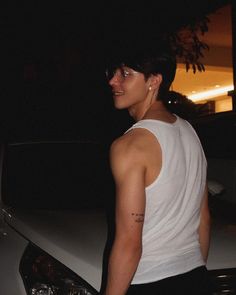 a young man standing in front of a white car at night with his head turned to the side