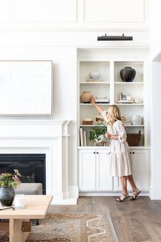 a woman standing in front of a fireplace with her hand up to the wall above it