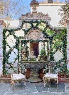 an outdoor fountain with two chairs around it and ivy growing on the wall behind it