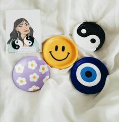 three buttons with smiley faces on them sitting on a white sheet next to a card