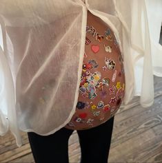 a pregnant woman's belly covered in stickers and plastic wrap, with her hands behind her back