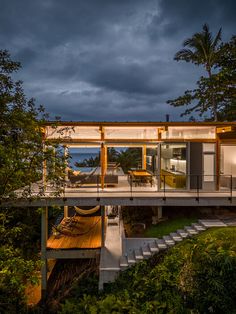 the house is surrounded by greenery and has a deck that leads to an outdoor lounge area