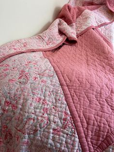 a pink and white quilted bedspread on top of a bed next to a wall