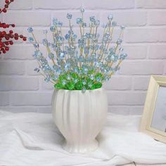 a white vase filled with blue flowers next to a framed photo and red berries on a table