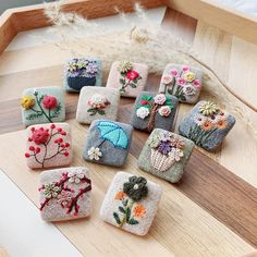 nine small handmade embroidered purses sitting on a wooden table next to some dried flowers