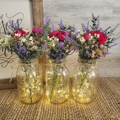 three mason jars filled with flowers sitting on a table next to a wooden frame and string lights