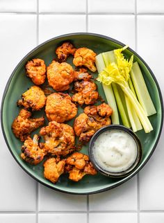 a green plate topped with cauliflower and celery next to a bowl of ranch dressing