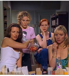 four women sitting around a table with drinks in front of them and one woman pointing at the camera