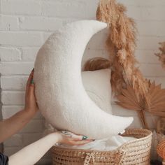 a person holding a large white pillow in front of a basket with feathers on it