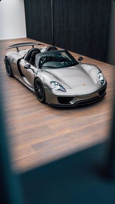 a silver sports car is parked in a room with wood flooring and black walls