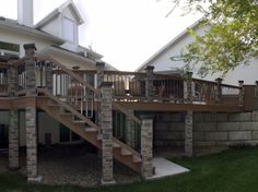 an outdoor deck with stone pillars and steps leading up to the back of a house