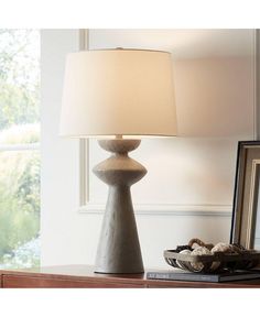 a table lamp sitting on top of a wooden table next to a framed photo and a mirror