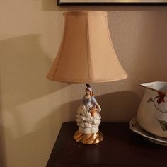 a lamp sitting on top of a wooden table next to a white pitcher and plate