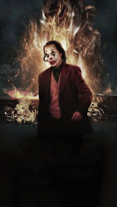 the joker is sitting in front of a large fire and demon face with his mouth open