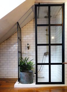 a bathroom with a glass shower door and wooden flooring, along with white tiled walls