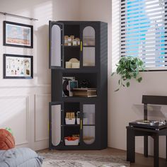 a living room with a black bookcase in the corner next to a window filled with plants