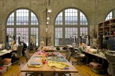 people are sitting at tables and working in an open room with large windows that look out onto the city