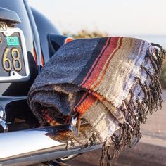 a plaid blanket on the back of a motorcycle parked by the beach in front of a car