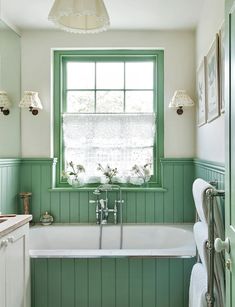 a bathroom with green painted walls and white bathtub in front of a large window