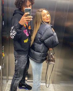 a man and woman taking a selfie in front of an elevator with their cell phones