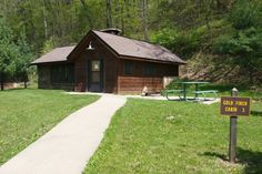 a small cabin sits in the middle of a grassy area next to a trail and picnic table