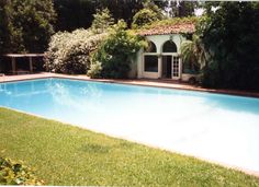 an empty swimming pool surrounded by greenery and trees in front of a house with a covered patio