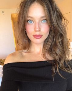 a woman with blue eyes is posing for the camera in a black off shoulder top