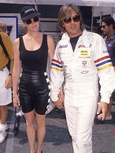 a man and woman dressed in racing gear walking down the street with people behind them