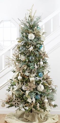 a decorated christmas tree with blue and white ornaments on it's base, in front of a staircase