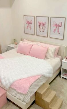 a white bed with pink pillows and two pictures on the wall next to it's foot steps