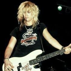 a man holding a white guitar in his right hand and wearing a black t - shirt