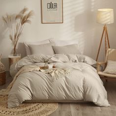 a bed with white linens and pillows in a room next to a chair, lamp and pictures on the wall