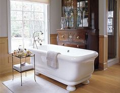 a large white bath tub sitting inside of a bathroom next to a wooden cabinet and window