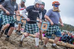 men in kilts carrying wooden planks down a muddy hill at a sporting event