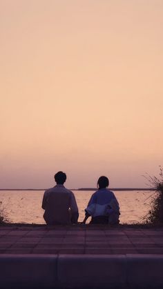 two people sitting on the ground watching the water