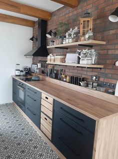 a kitchen with black cabinets and wooden shelves next to a brick wall that has open shelving above it