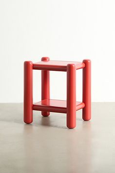 a small red table sitting on top of a cement floor next to a white wall