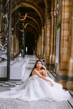 a woman is sitting on the ground in a white dress and posing for a photo