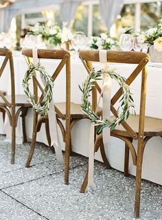 two wooden chairs sitting next to each other on top of a table with greenery wreaths