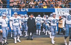 the cowboys are walking out onto the field with their football uniforms on and people in the stands watching