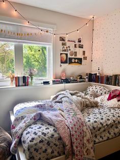 an unmade bed sitting next to a window in a room with bookshelves