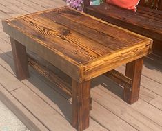 a wooden table sitting on top of a wooden deck next to a bench and flowers