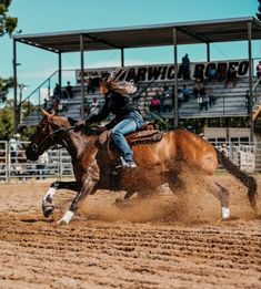 a woman riding on the back of a brown horse in a dirt field next to a crowd