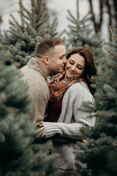 a man and woman standing next to each other in front of christmas tree farm trees