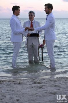 three men in white suits shaking hands on the beach