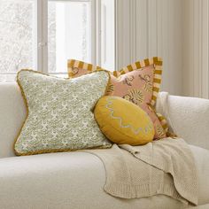 a white couch with pillows on top of it next to a blanket and window sill