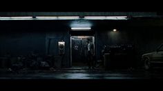 two men standing in the doorway of a dark building at night with their cars parked nearby