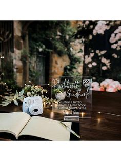 an open book sitting on top of a wooden table next to a camera and flowers