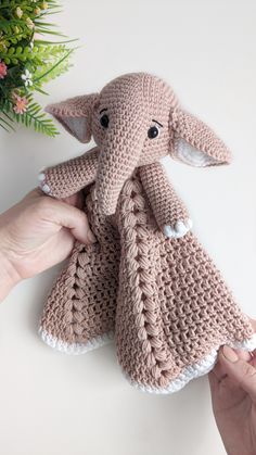 an elephant stuffed animal being held by someone's hand on a white surface with flowers in the background